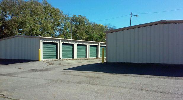 A row of outdoor, drive-up access storage units with green doors.