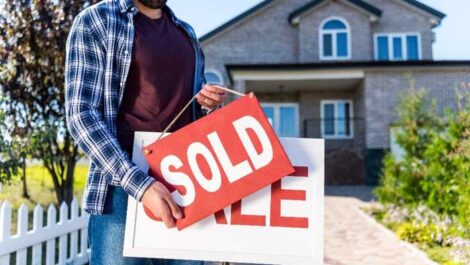 Man replacing a for sale sign with a sold sign.