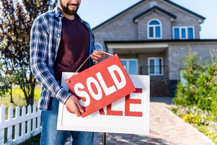 Man replacing a for sale sign with a sold sign.
