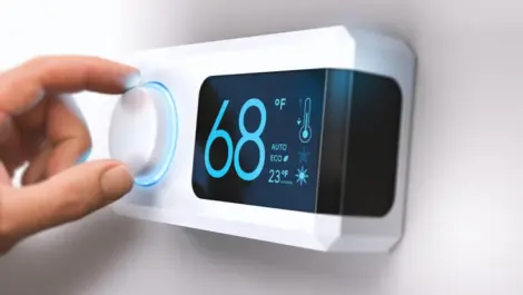 A person adjusts a thermostat mounted on the wall