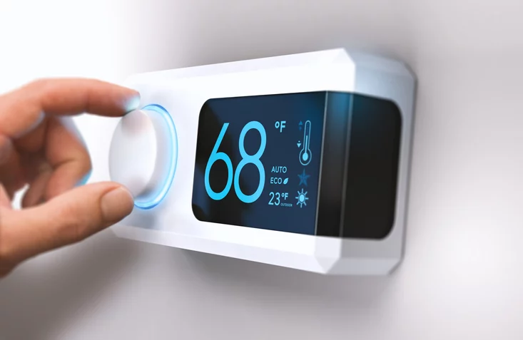 A person adjusts a thermostat mounted on the wall