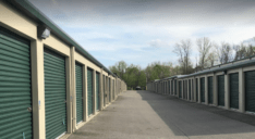 A row of outdoor, drive-up access storage units with green doors.
