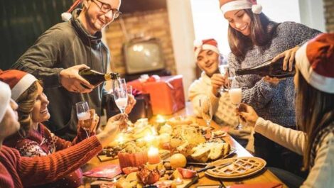 Group of adults wearing Santa hats pouring champagne at the dinner table.