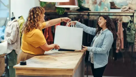 A woman hands a shopping bag to a customer in a small business after purchase