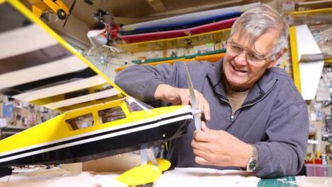 older gentleman fixing the propeller on a yellow and black model airplane in his workshop