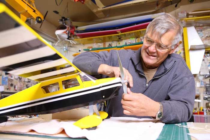 older gentleman fixing the propeller on a yellow and black model airplane in his workshop