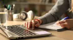 Person searching on a computer next to a notepad.
