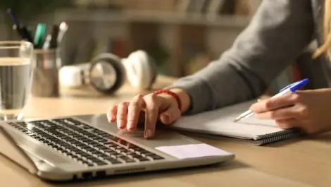 Person searching on a computer next to a notepad.