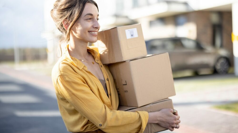 A woman in a yellow shirt carries three small boxes in a stack