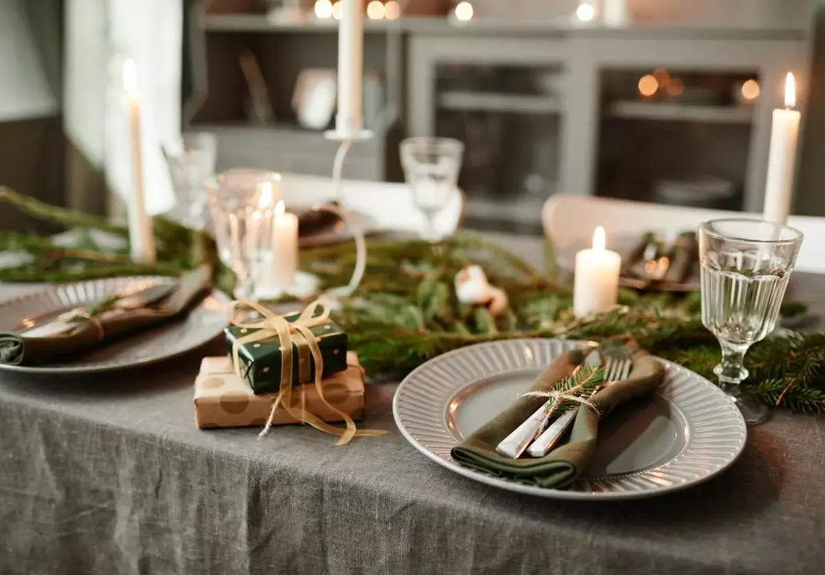 Dishes and place settings are arranged on a table next to small gifts and festive greenery