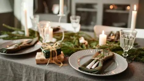 Dishes and place settings are arranged on a table next to small gifts and festive greenery