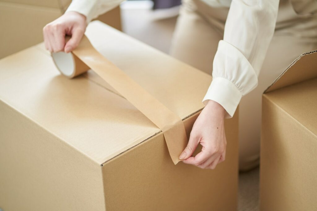 A person seals a cardboard box with packing tape