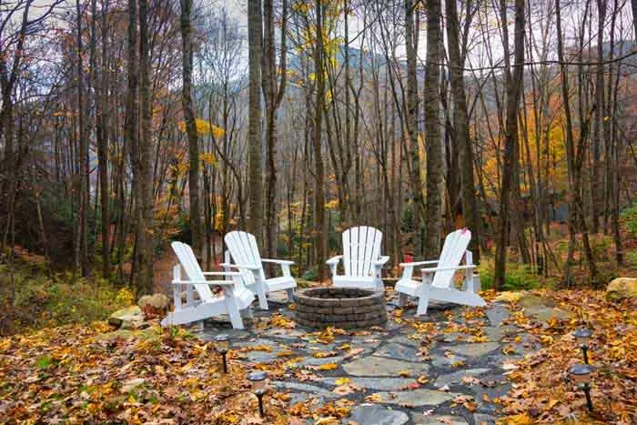 Stone fire pit with Adirondack chairs surrounding it.