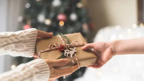 Woman in sweater giving a wrapped Christmas gift box to child.