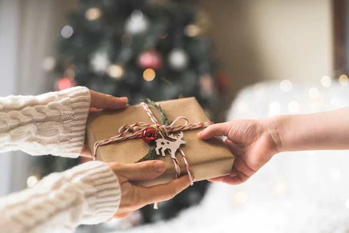 Woman in sweater giving a wrapped Christmas gift box to child.