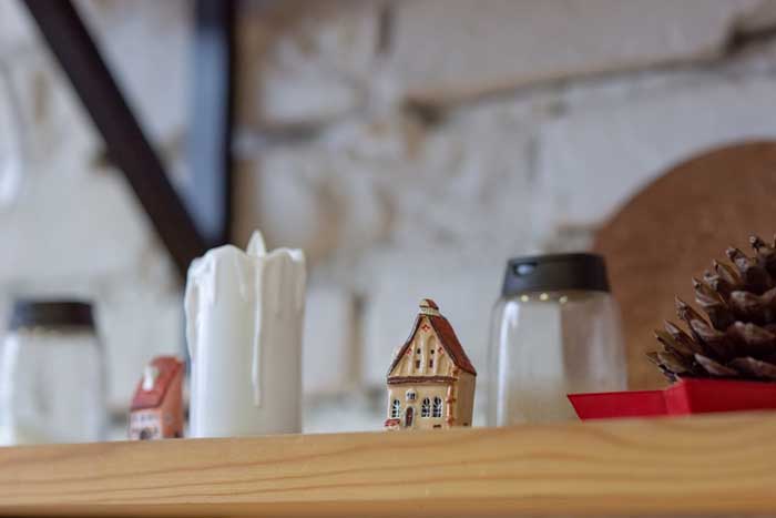 Wooden kitchen shelf with Christmas ceramic figurines of cute antique colorful houses, big cedar cone and big white candle.