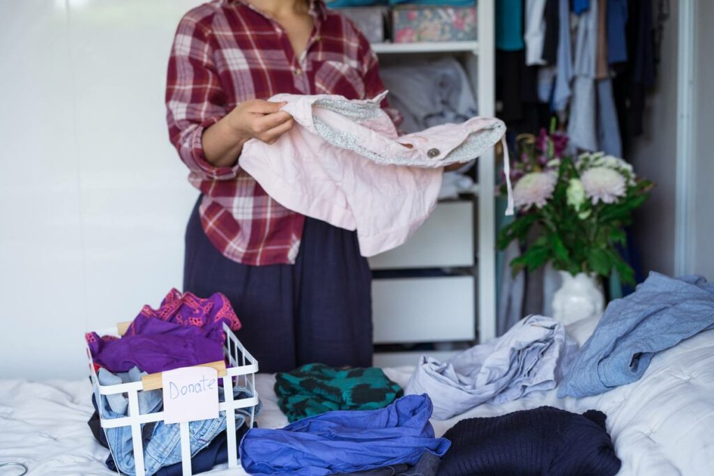 A woman stands by a bed sorting through clothing to donate.