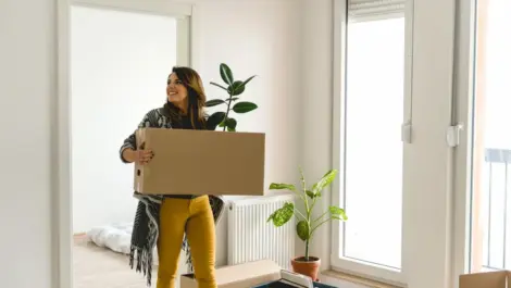 A woman carries a box into an empty apartment.