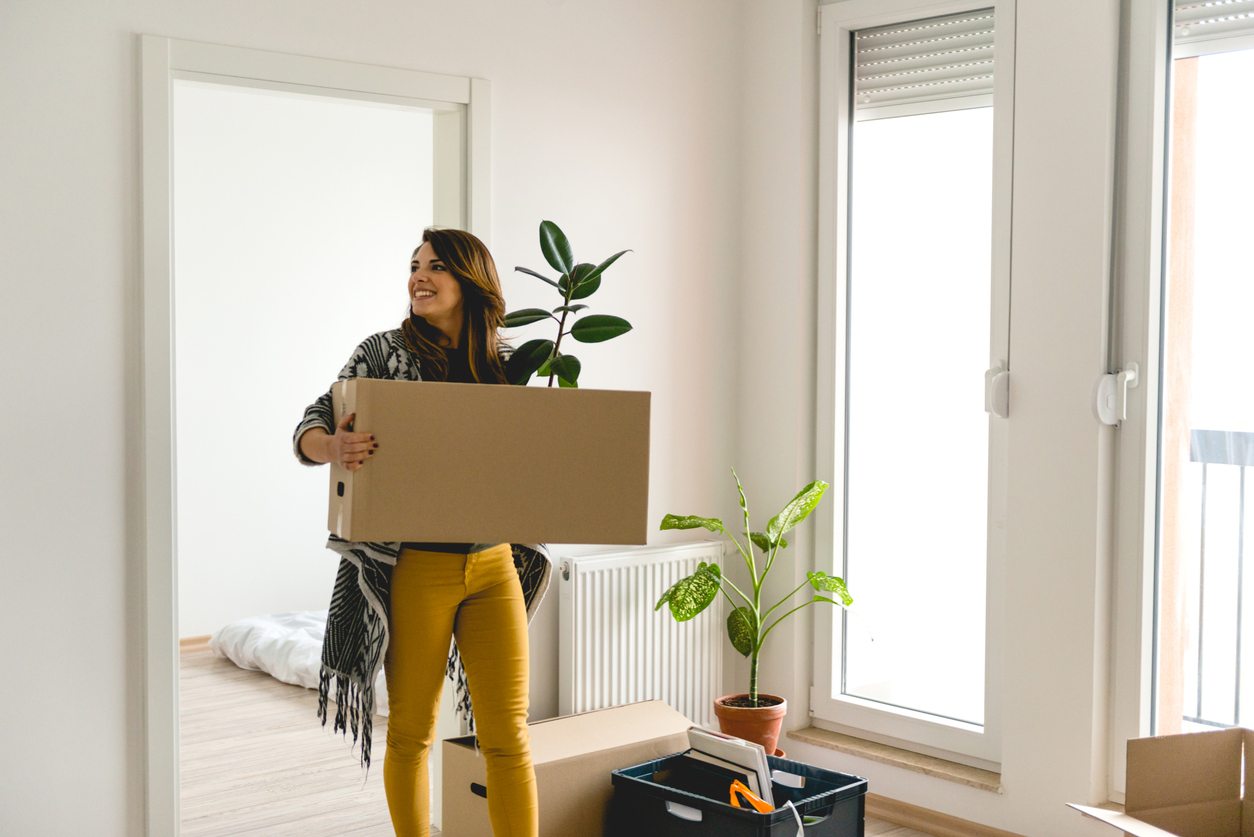 A woman carries a box into an empty apartment.