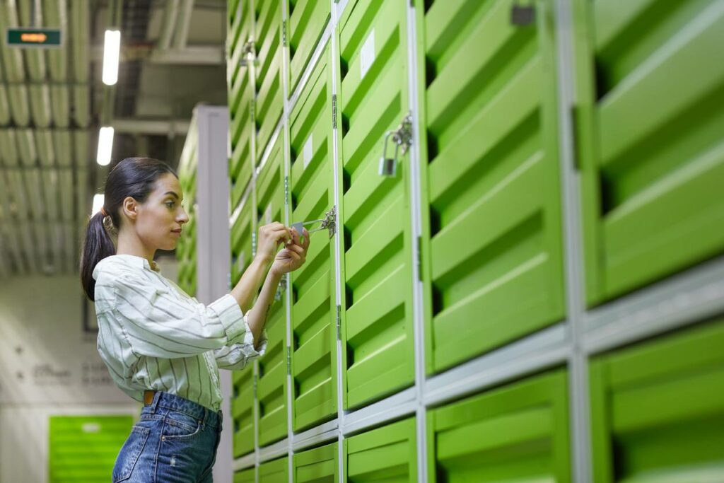 A woman standing in front of a green storage locker unlocks the lock.