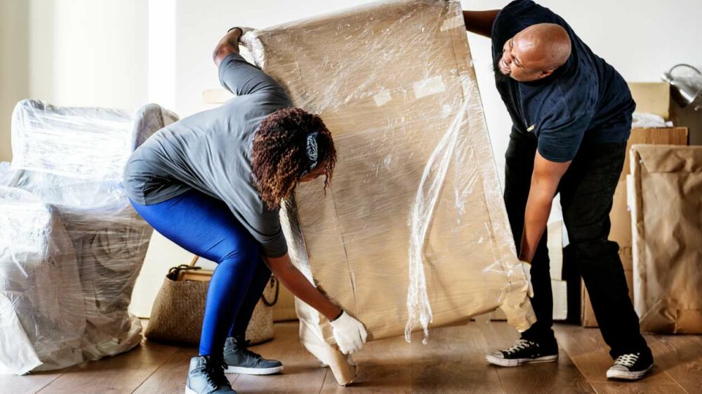 A couple moving a wooden dresser covered in plastic covering