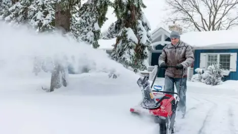 A man clears a driveway covered in snow using a red snow blower