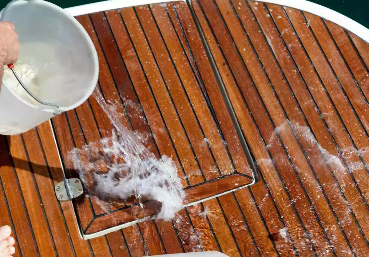 A bucket of water is dumped onto the wooden deck of a boat