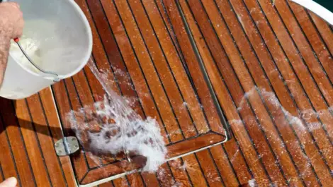 A bucket of water is dumped onto the wooden deck of a boat