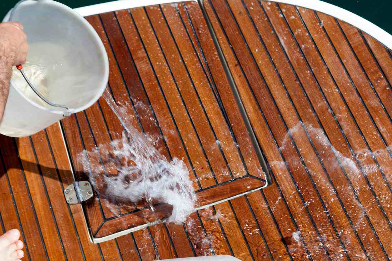 A bucket of water is dumped onto the wooden deck of a boat