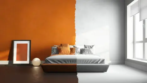 A bedroom with one-half orange walls, dark flooring, and extra décor and one-half white walls, white bedding, and floors with no extra décor