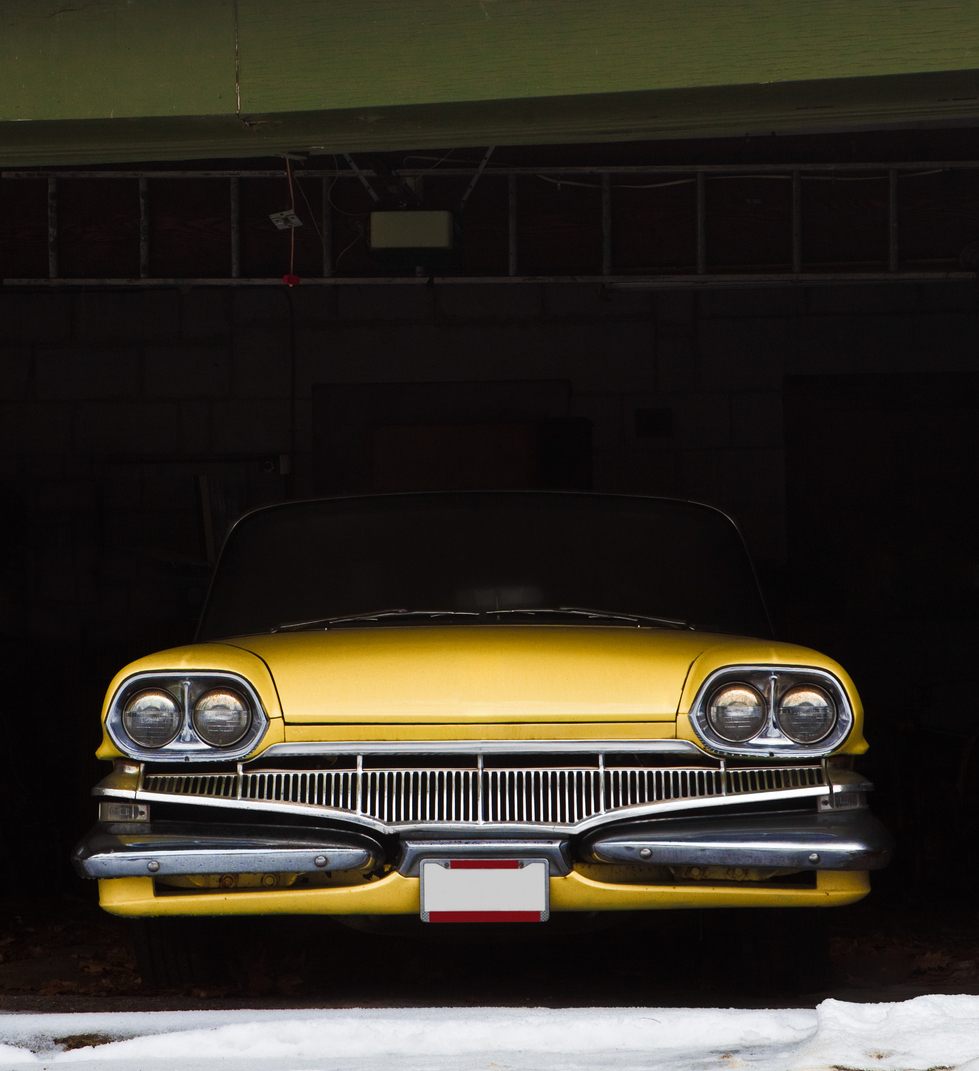 A yellow classic car sits in a dark storage unit