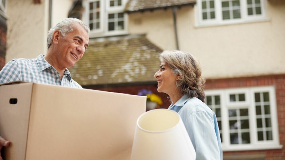 An older couple carries things out of their home while downsizing