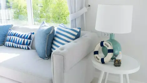 Living room decorated for vacation rental with a cozy, large white couch, white side table and throw pillows in a variety of shades of blue.