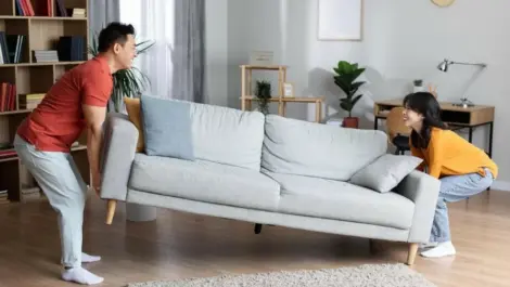 Two homeowners happily moving a couch.