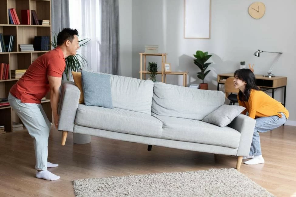 Two homeowners happily moving a couch.