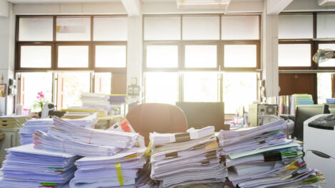 Several stacks of paper documents and files on a messy desk.