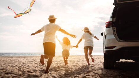A happy family runs onto the beach after planning a road trip along the coast.
