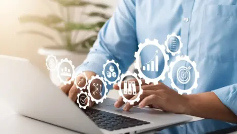 A graphic with a man typing on a laptop and gears floating around.