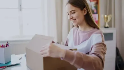 A college student is packing her dorm desk into a brown box.