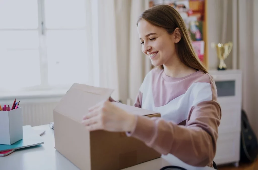 A college student is packing her dorm desk into a brown box.