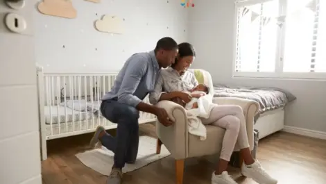 Parents hold their newborn on a bed in the nursery.
