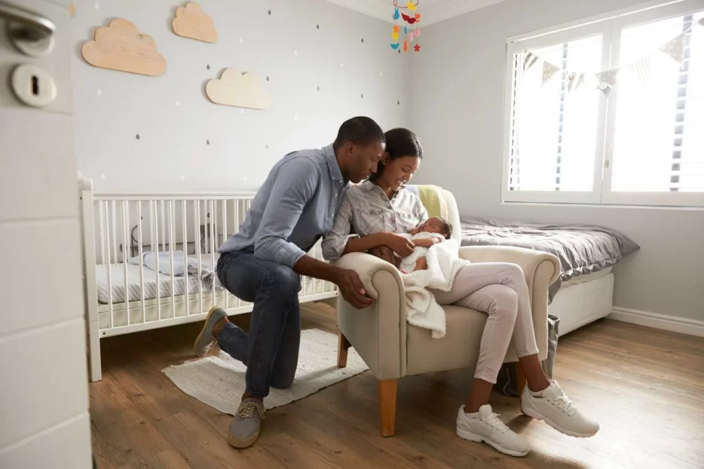 Parents hold their newborn on a bed in the nursery.