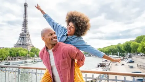 A couple posing together on a bridge over the Seine River with the Eifel Tower.